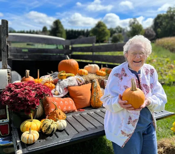 Senior woman holding a pumpkin by a truck full of pumpkins