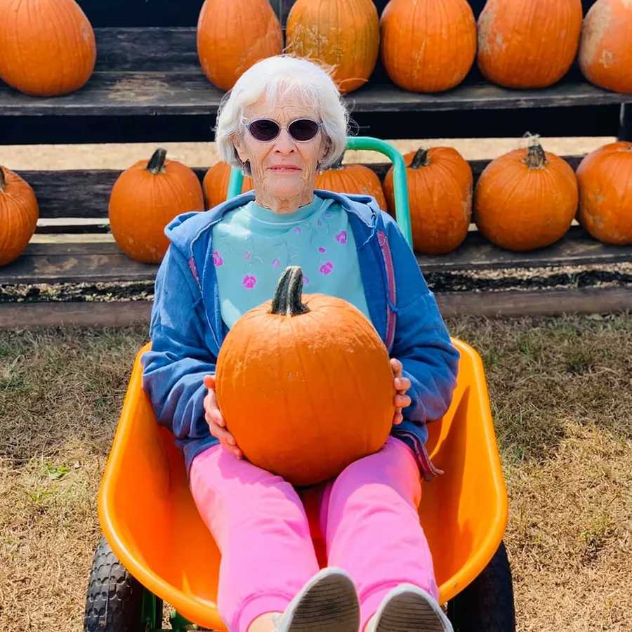 Fun pumpkin patch photo: senior woman sitting in a wheelbarrow with a pumpkin