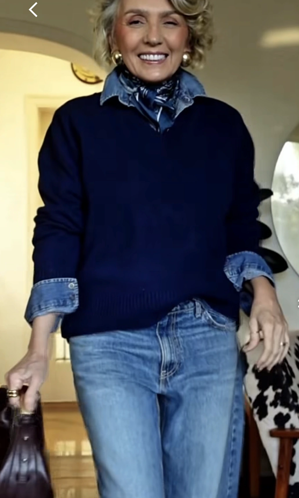 Woman over 50 wearing a navy sweater layered over a denim shirt with jeans