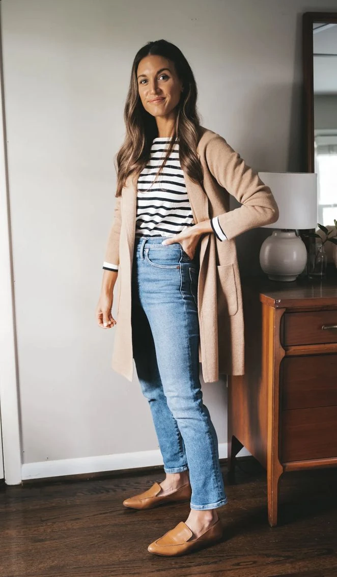 Camel long cardigan over a striped top with jeans and tan flats indoors