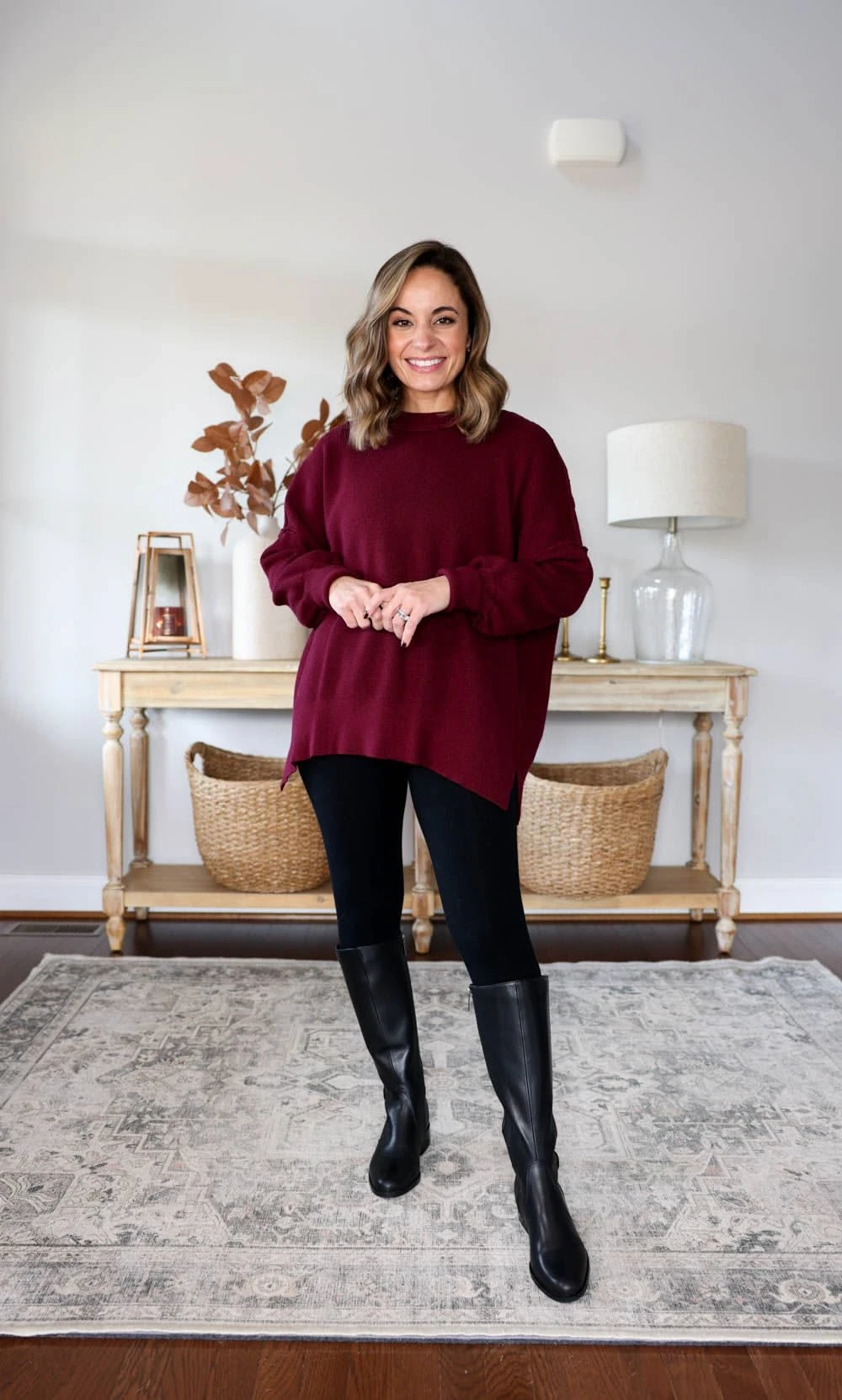 Burgundy oversized sweater tunic with black leggings and black knee boots indoors
