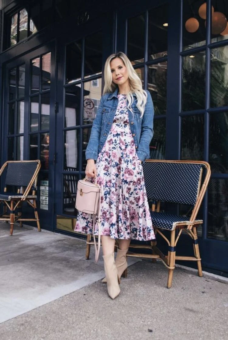 Denim jacket over a floral midi dress with light boots outside a cafe