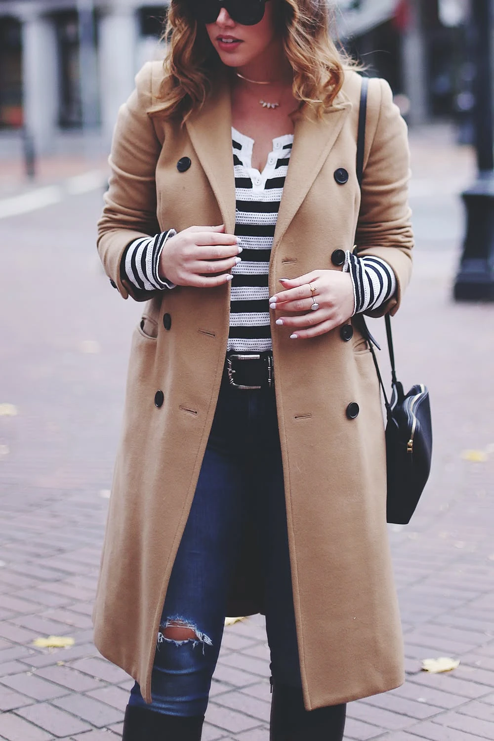 Camel coat over a striped top with ripped jeans on a city street