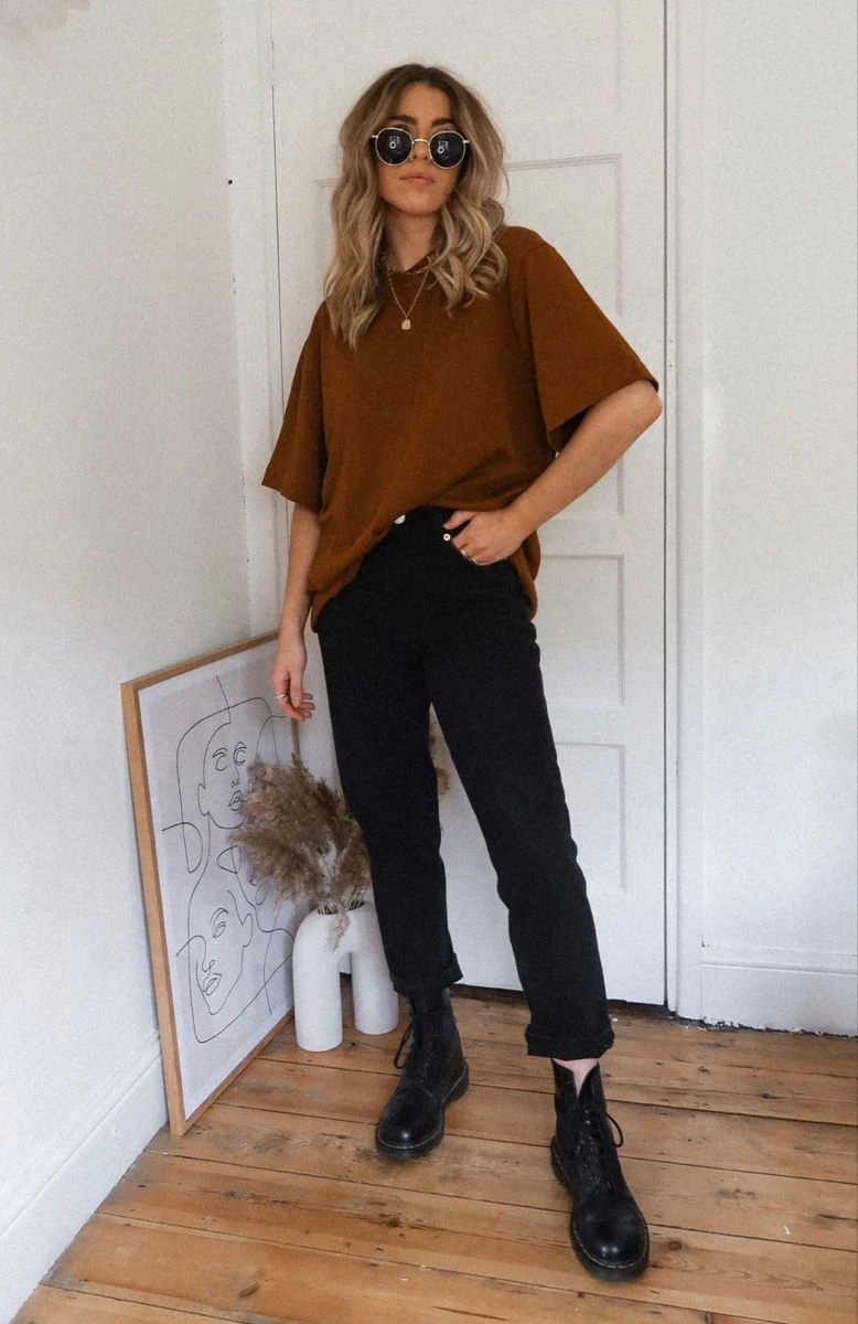 Rust brown loose top with black jeans and black boots indoors