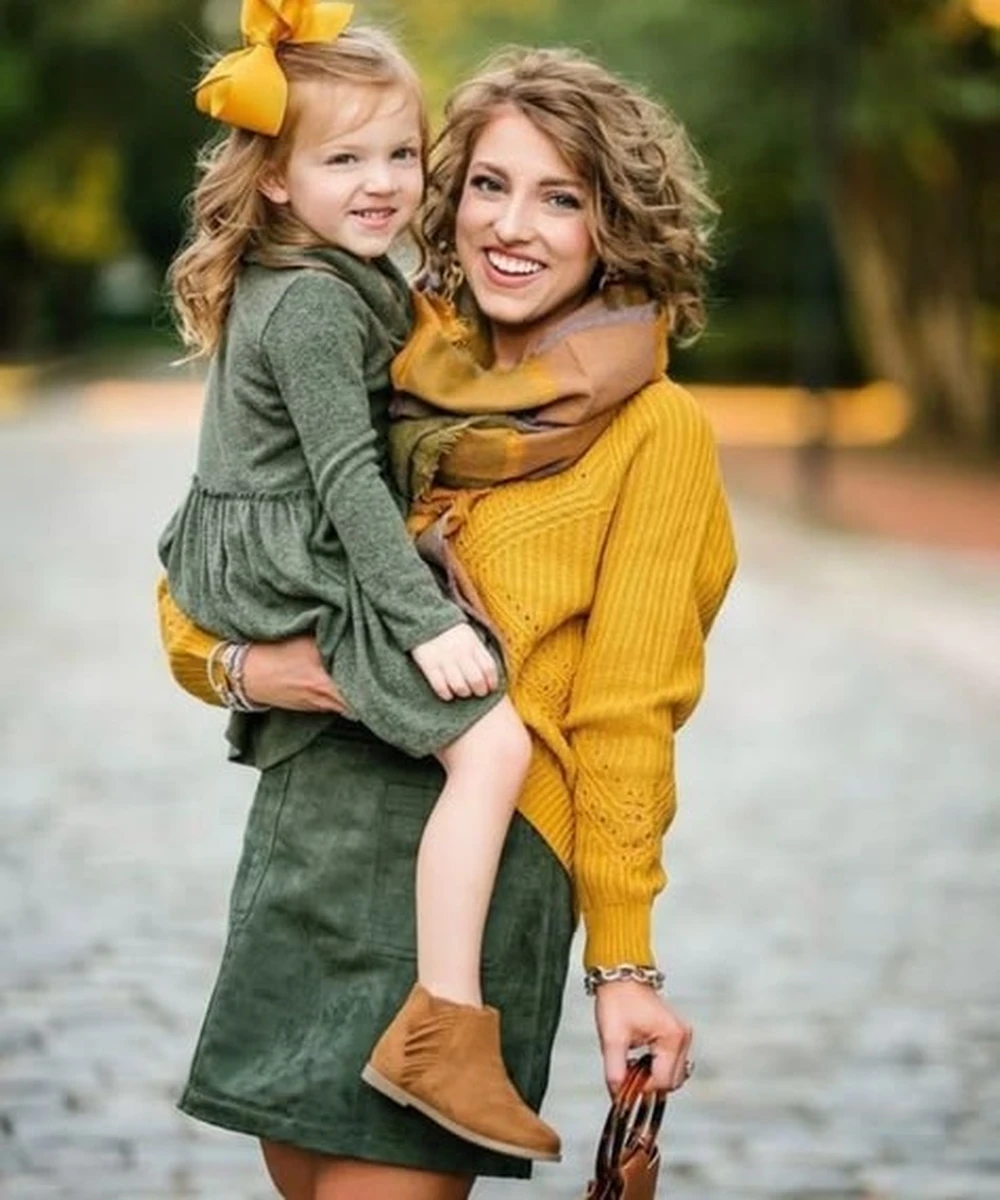 Mother in a mustard sweater and olive skirt holding a young girl in an olive dress