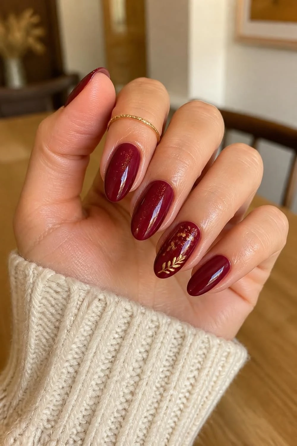 Cranberry oval nails with a gold leaf accent and cream knit sleeve