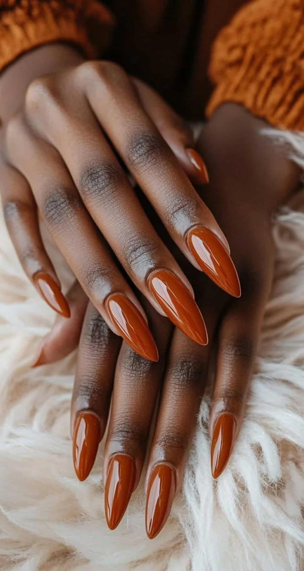 Glossy burnt orange almond nails on a soft knit