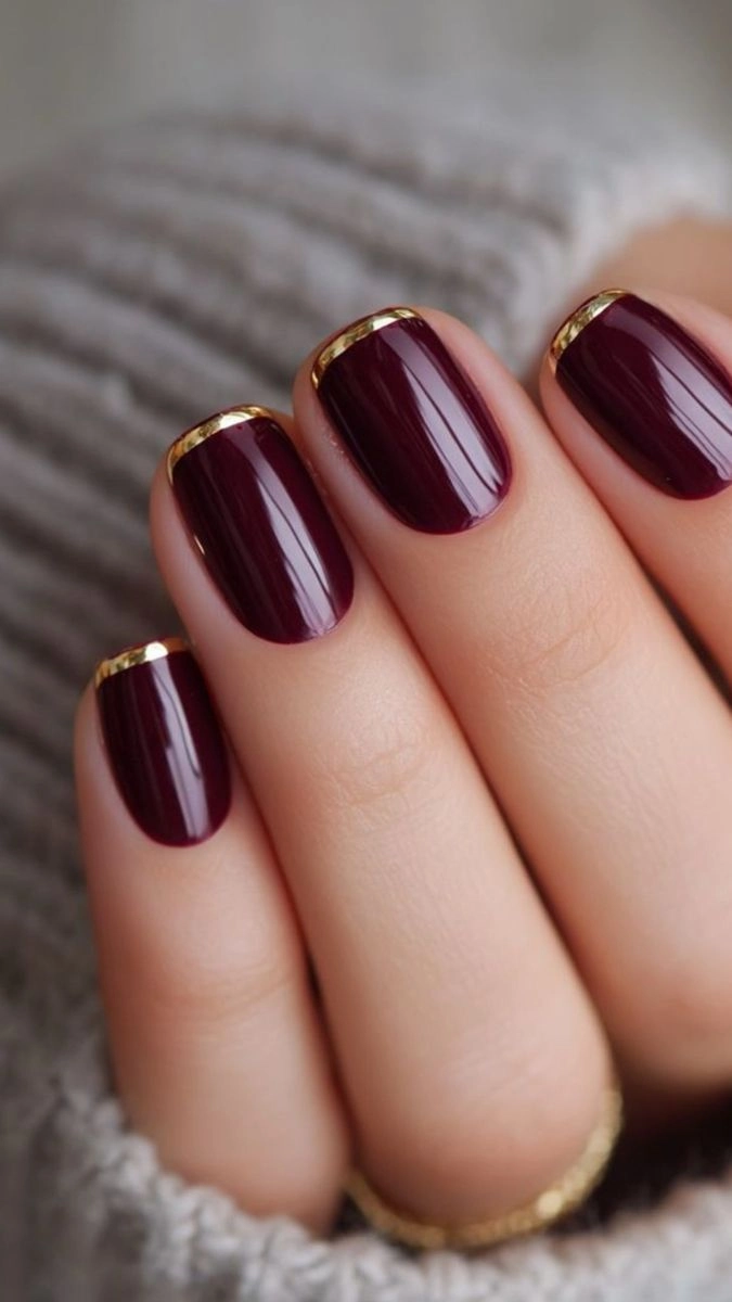 Short wine nails with a thin gold edge at the cuticle