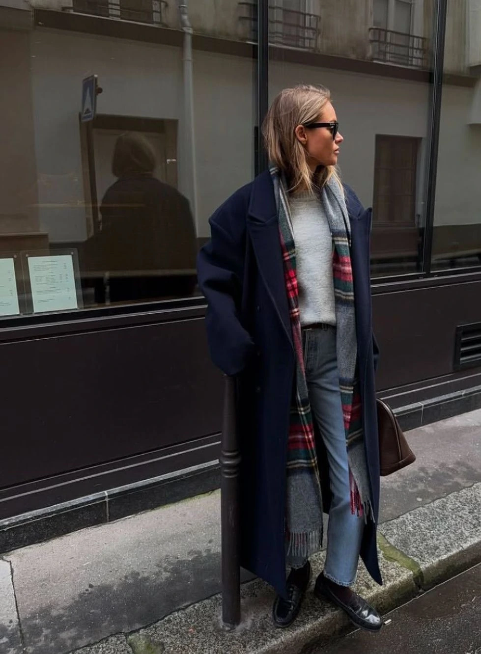 Woman in a navy coat with a checked scarf and grey trousers