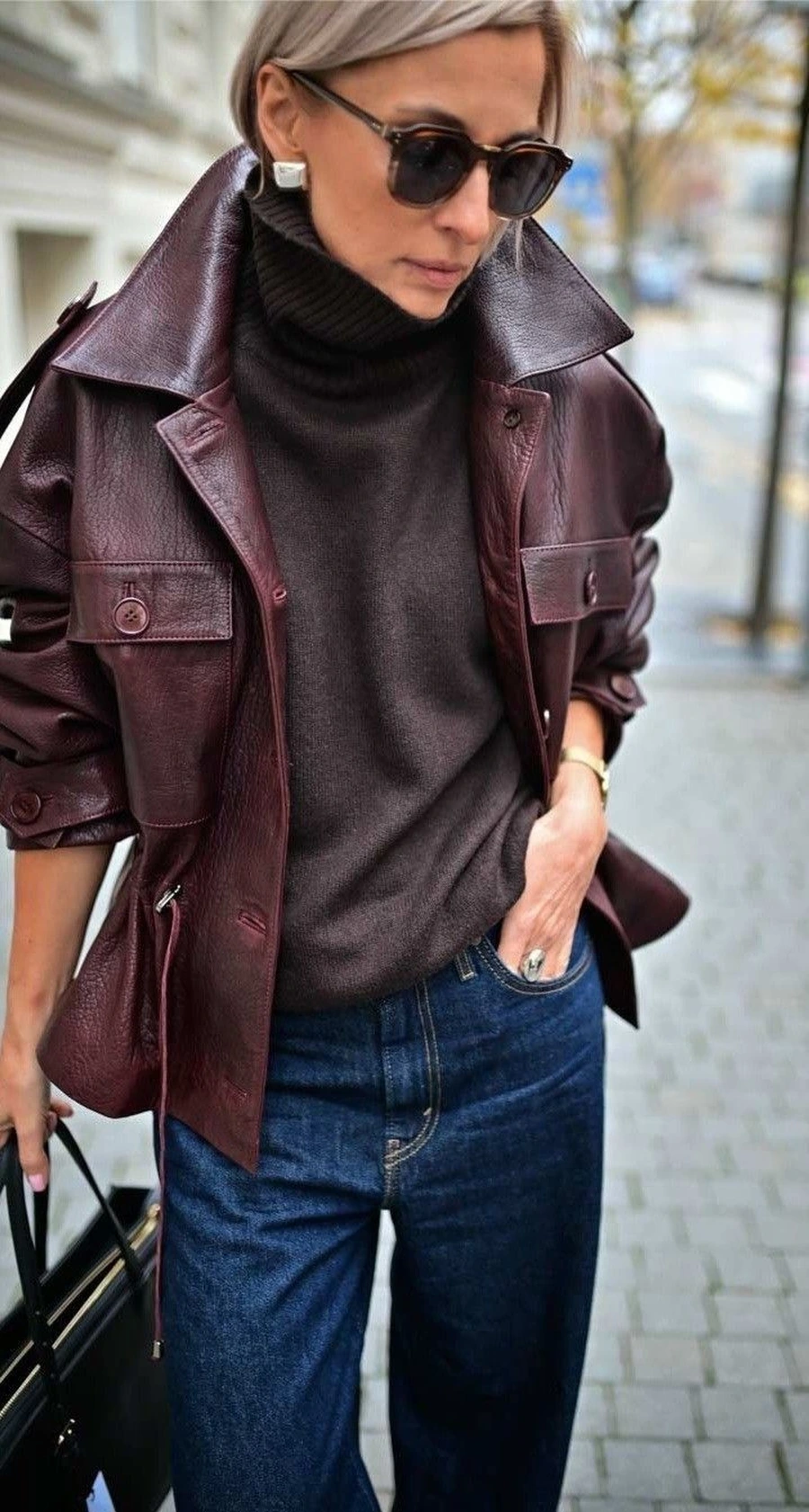 Woman wearing an oxblood leather jacket over a black midi dress with boots