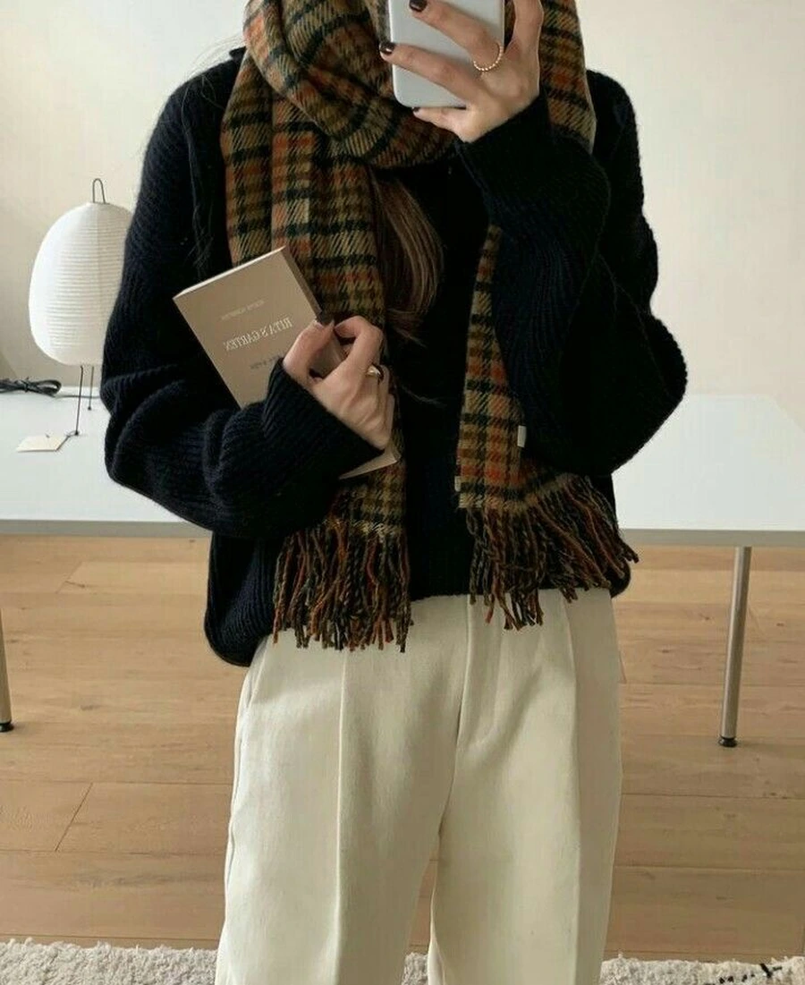 Woman in a chunky knit sweater with a tartan scarf and cream trousers