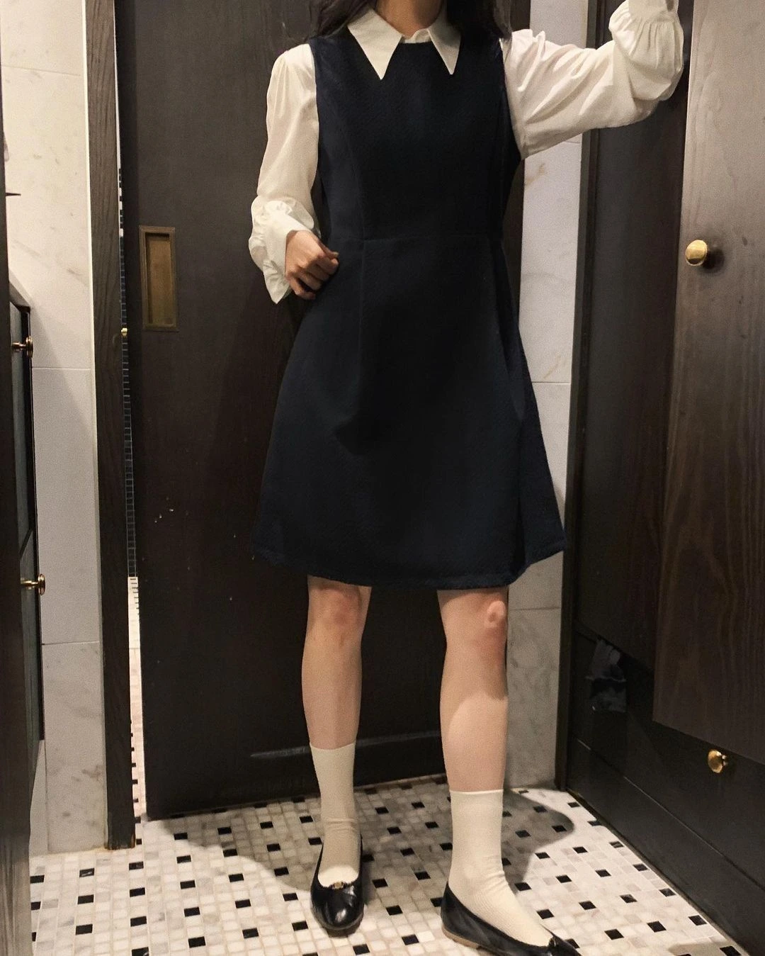 Woman in a black pinafore dress over a white blouse with loafers