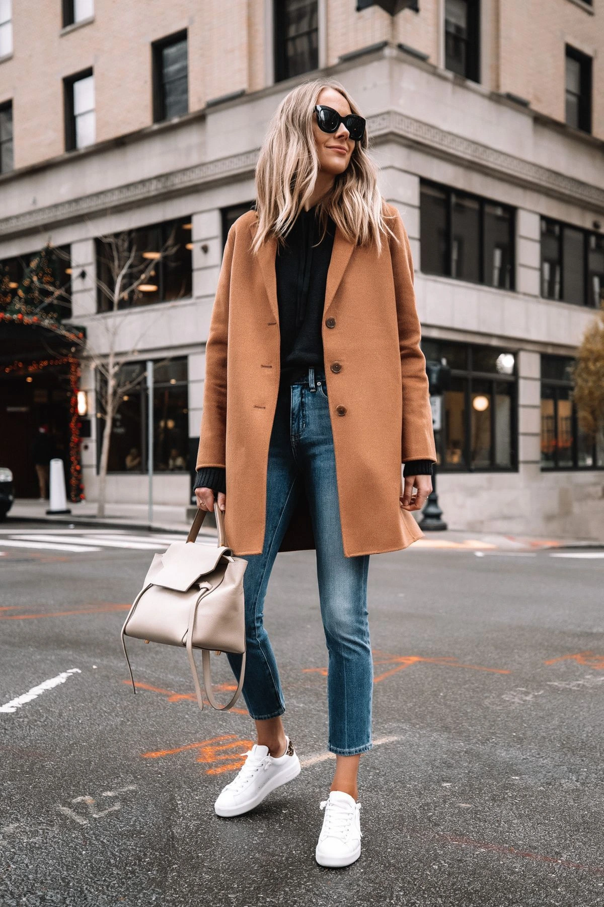 Woman wearing white sneakers with a camel coat and straight jeans for fall