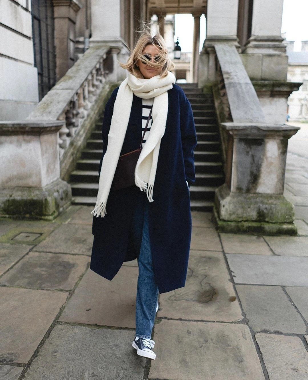 Woman wearing sneakers with a checked scarf, navy coat, and jeans