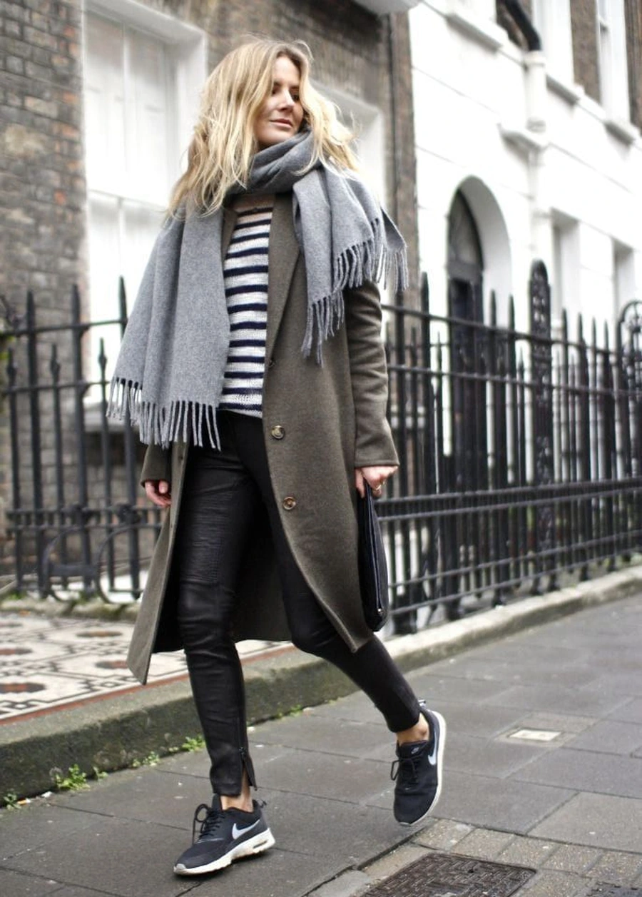 Woman wearing sneakers with a chunky scarf, sweater dress, and coat