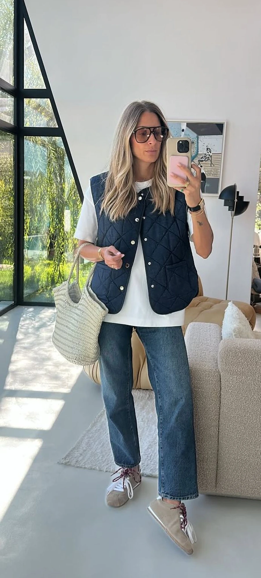 Woman wearing sneakers with a quilted vest, sweater, and dark jeans
