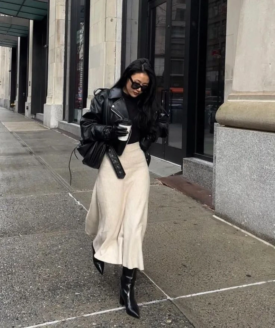 Woman wearing a leather jacket with a cream midi skirt and ankle boots