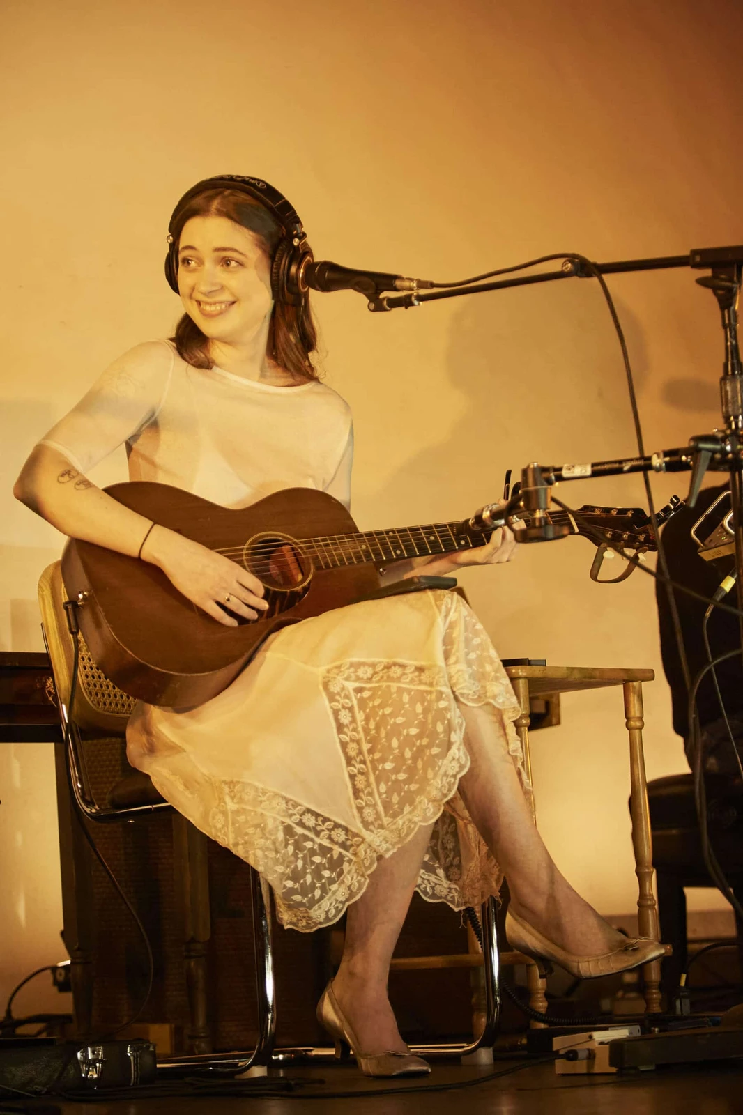 Lizzy McAlpine concert outfit: cream lace dress with guitar, seated