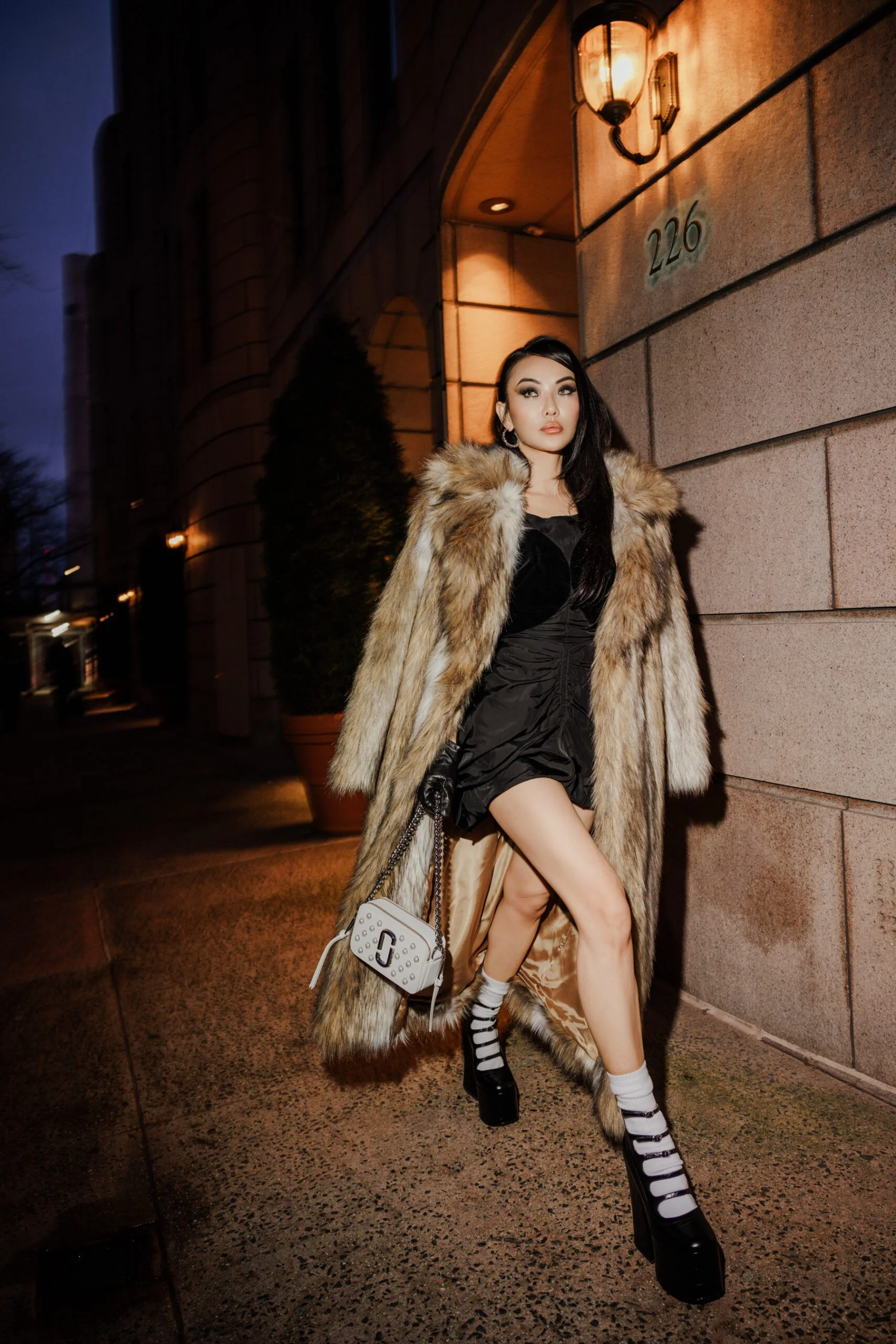 Tan fur coat over black dress on a night city street, mob wife outfit