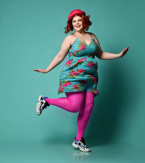 Turquoise floral mini dress with hot pink tights and chunky sneakers mid-jump