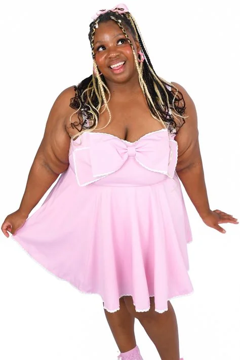 Pink skater dress with a giant bow and blonde braids, smiling at the camera