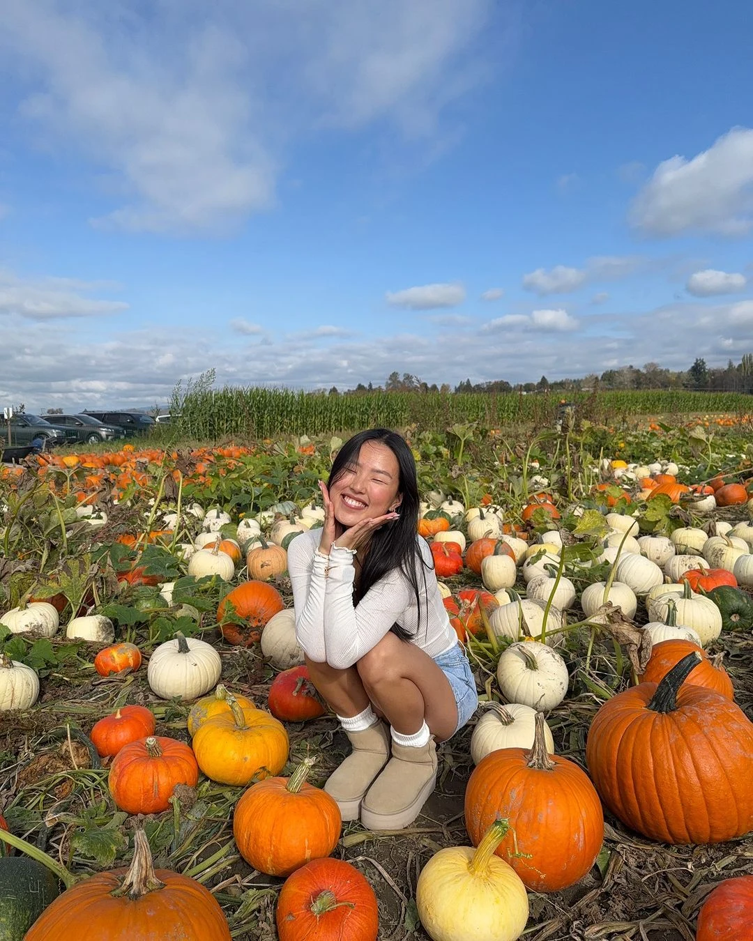 Fall pumpkin patch outfit: white top with denim shorts and tan boots among pumpkins