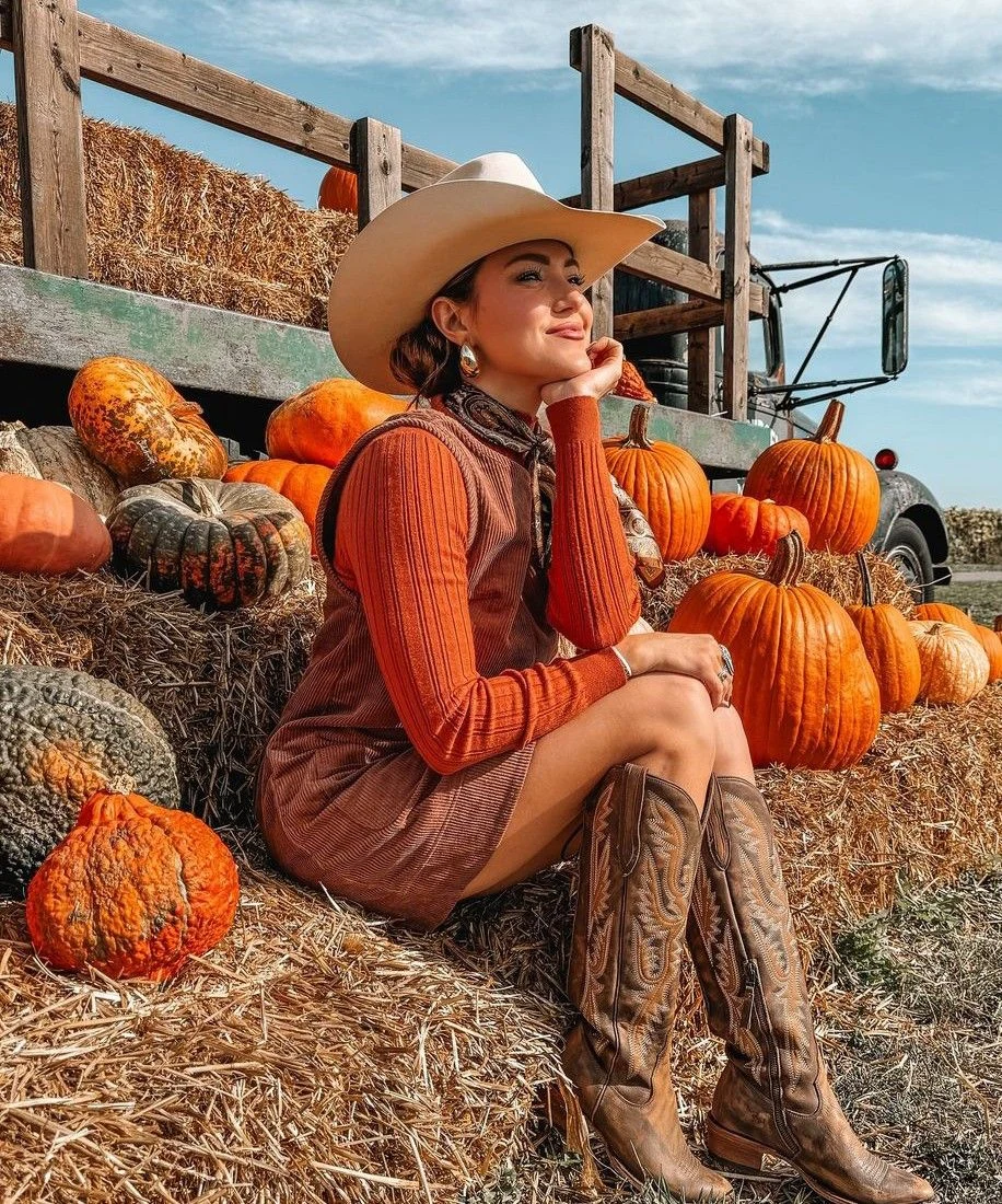 Fall pumpkin patch outfit: rust orange dress with cowboy boots and hat on hay bales