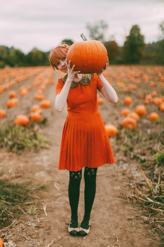Fall pumpkin patch outfit: orange pleated dress with patterned tights holding a pumpkin