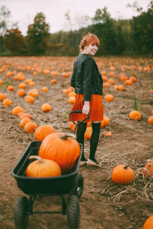Fall pumpkin patch outfit: black jacket with orange mini skirt pulling a pumpkin wagon