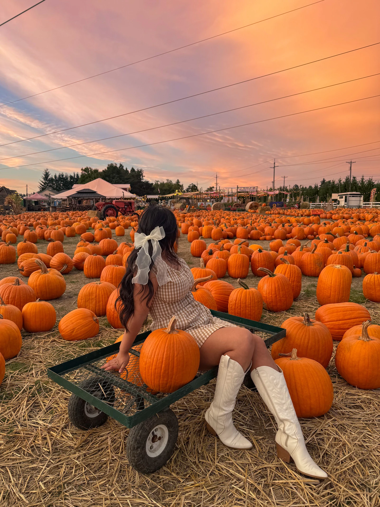 Fall pumpkin patch outfit: gingham romper with white knee-high boots on a wagon at sunset