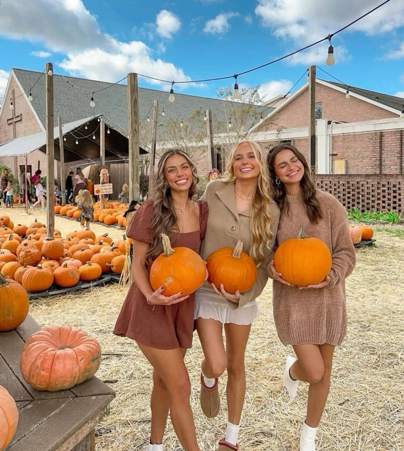Fall pumpkin patch outfits: three friends in rust and brown dresses holding pumpkins