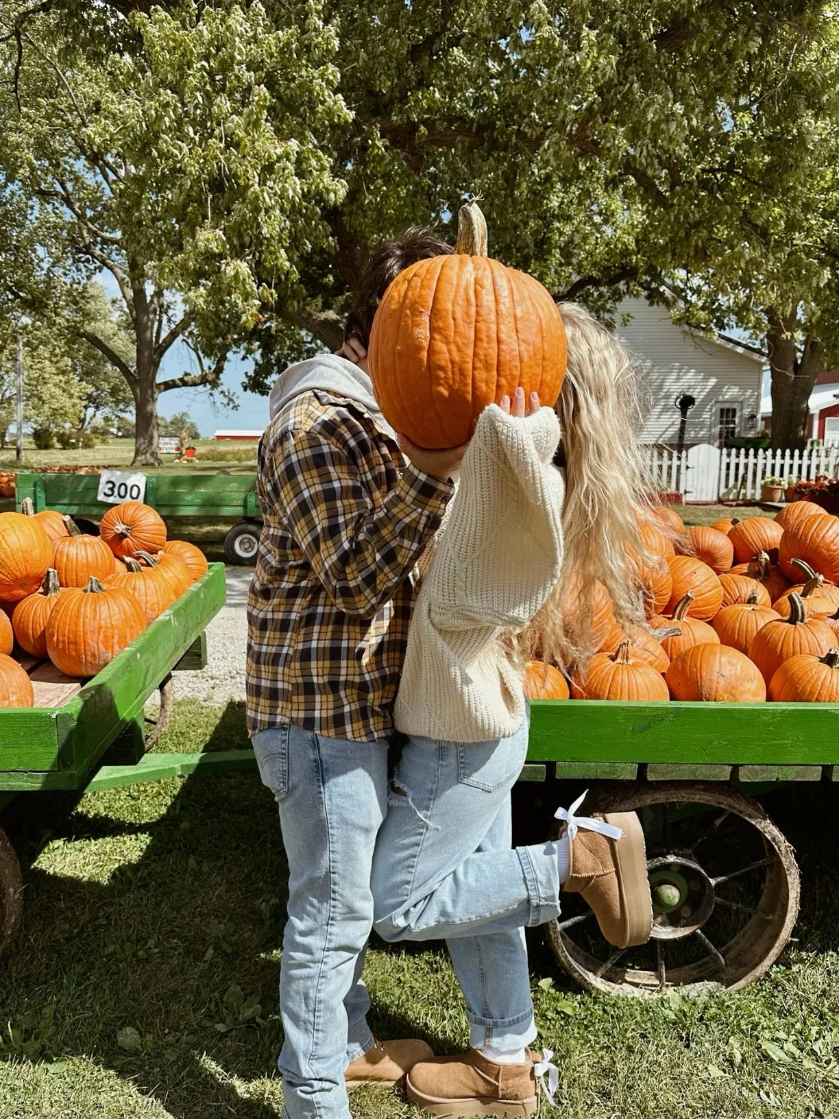 Fall pumpkin patch outfit: plaid flannel shirt and faded jeans holding a giant pumpkin