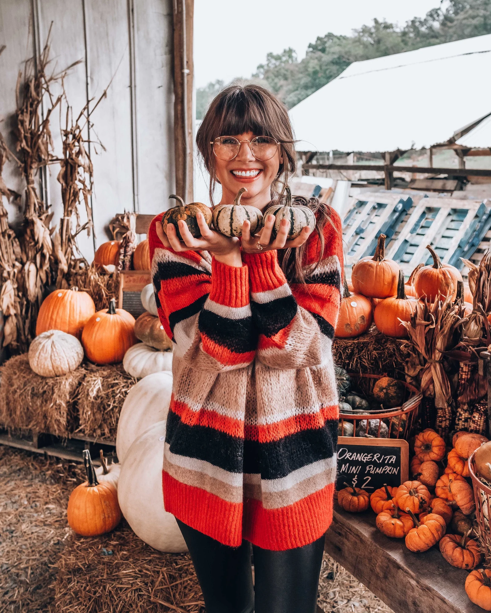 Fall pumpkin patch outfit: red striped cardigan holding gourds at a farm stand