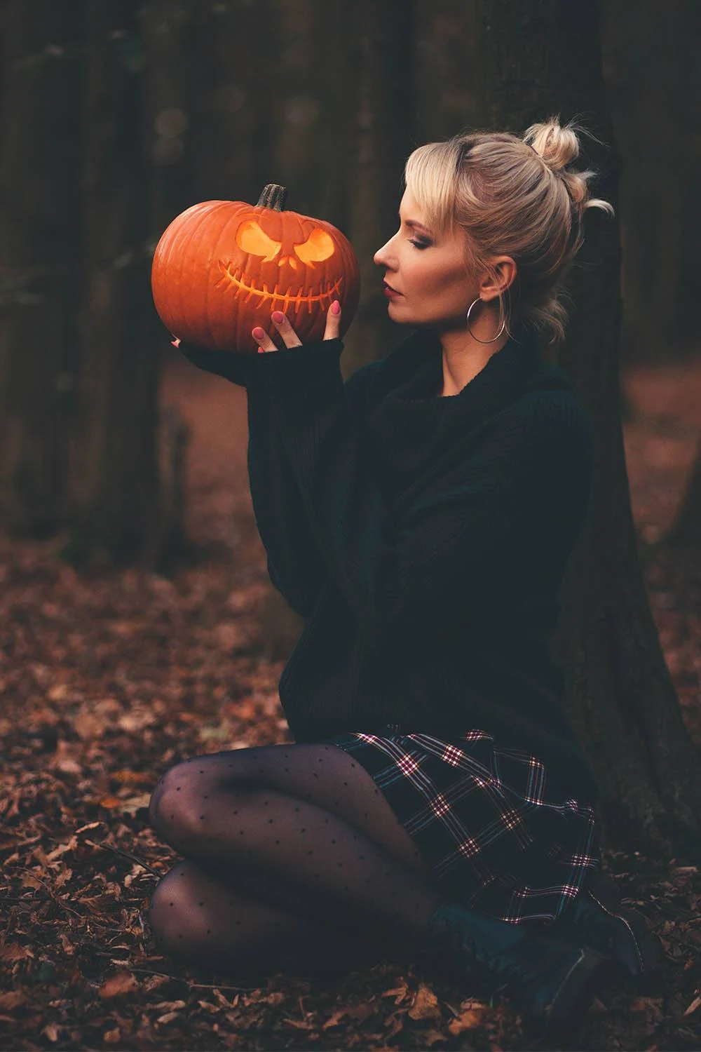 Fall pumpkin patch outfit: black sweater with plaid mini skirt holding a jack-o-lantern