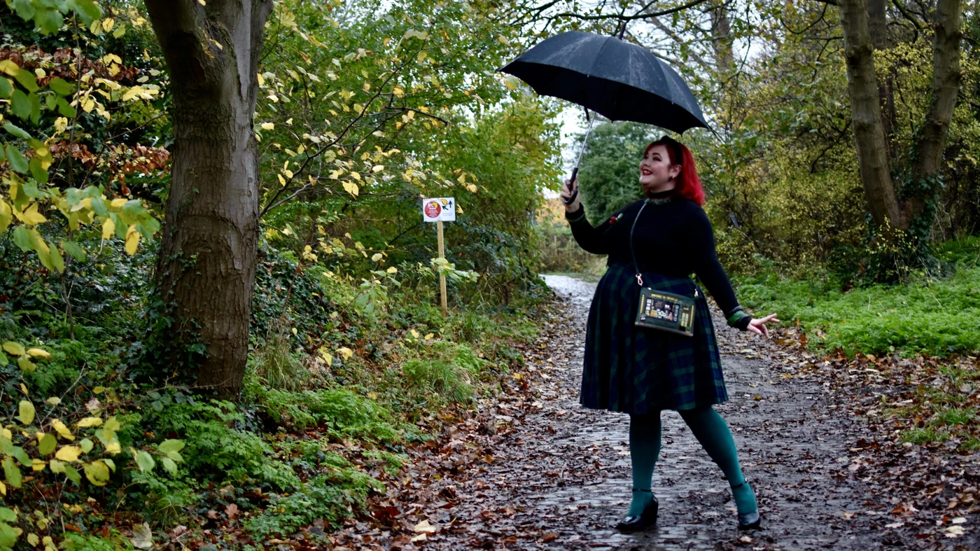 Plus-size woman in a black turtleneck, dark plaid skirt and teal tights with a black umbrella