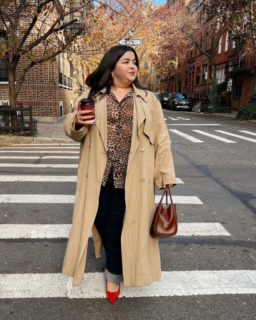 Plus-size woman in a beige trench coat, animal-print top and red heels at a crosswalk