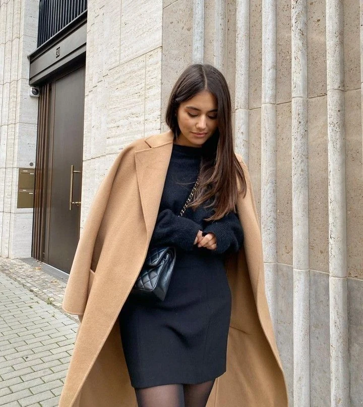 Petite woman wearing little black dress under a camel coat, cut short for Thanksgiving
