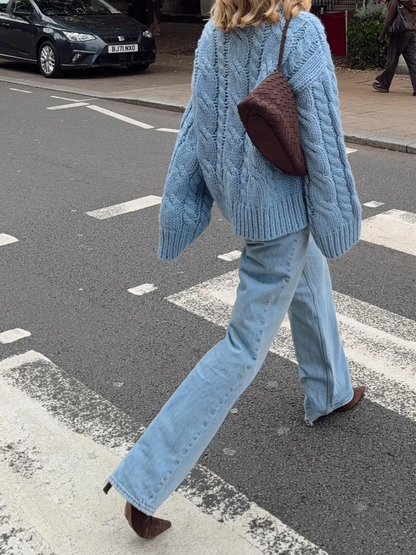 Woman wearing a dusty blue sweater with light wash wide leg jeans and a brown crossbody bag