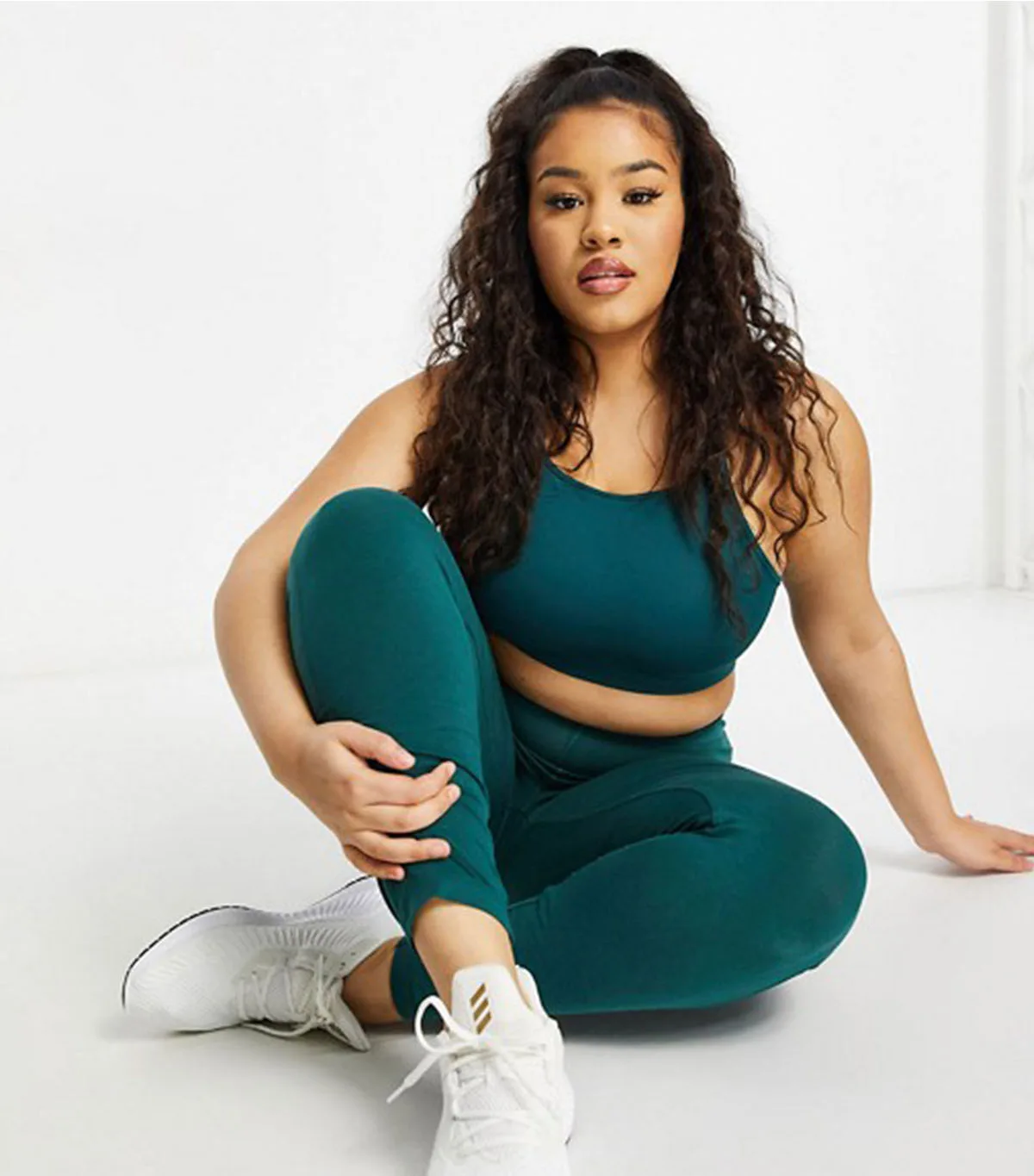 Plus size woman sitting in teal green workout set, sports bra and leggings
