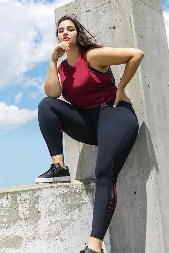 Curvy woman sitting on a concrete ledge in maroon tank top and black leggings