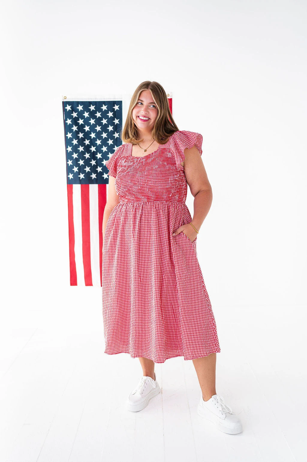 Plus size woman in red gingham midi dress in front of American flag