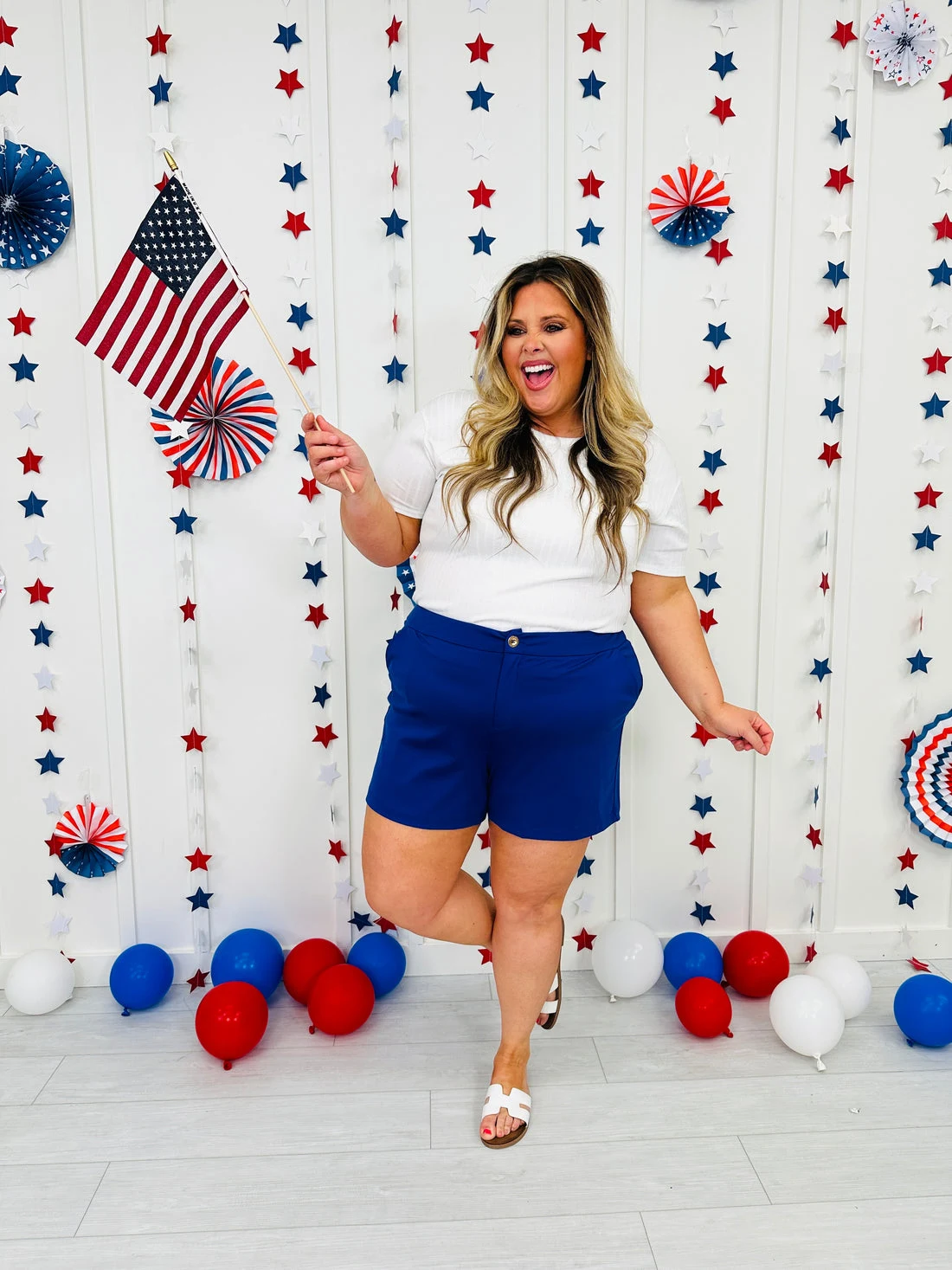 Plus size woman in white t-shirt and royal blue shorts holding American flag