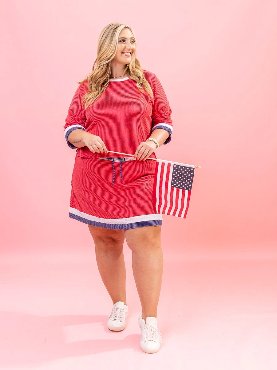 Plus size woman in red striped dress with navy and white trim holding flag