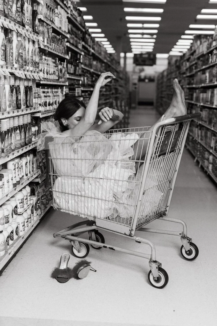 Bride riding inside a shopping cart down a supermarket aisle