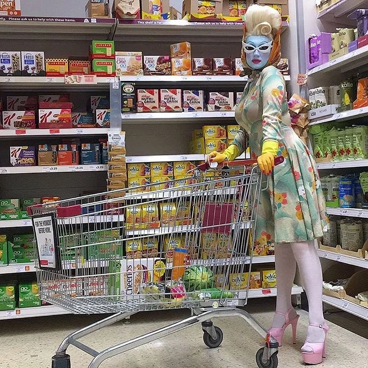 Woman in a floral dress with a face mask pushing a shopping cart