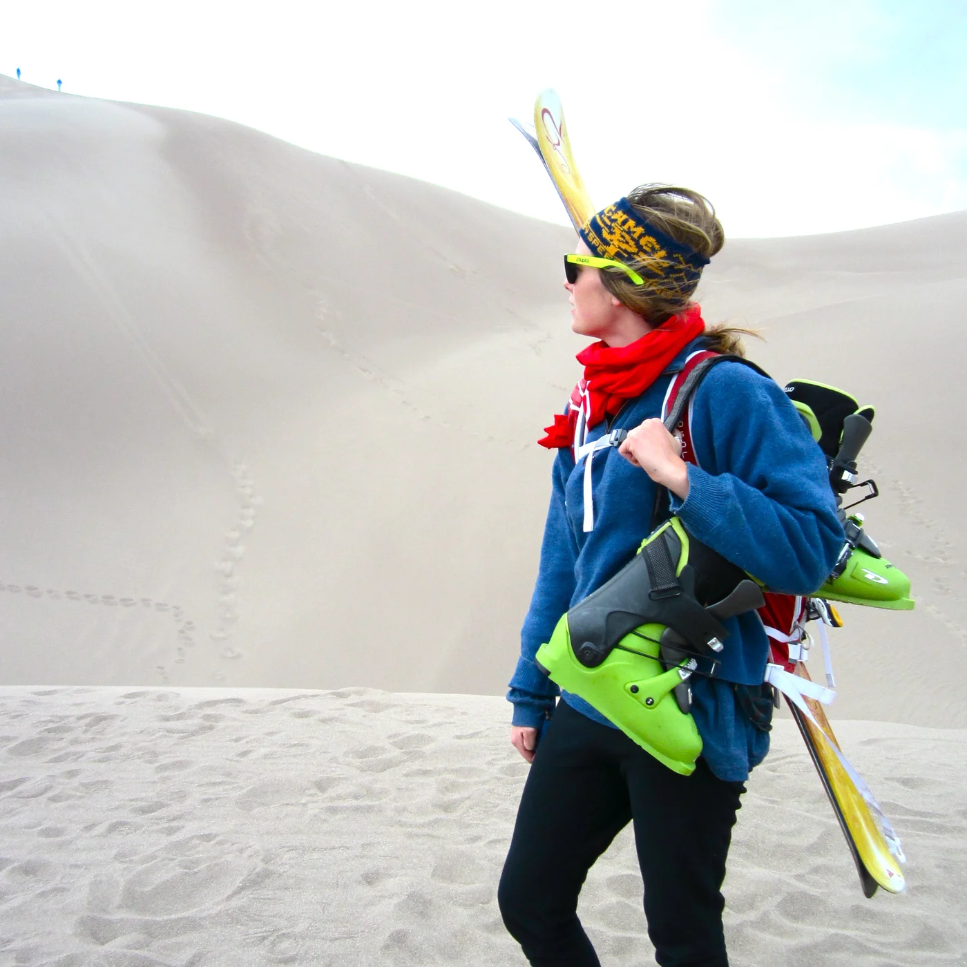 Woman carrying skis walking on sand dunes